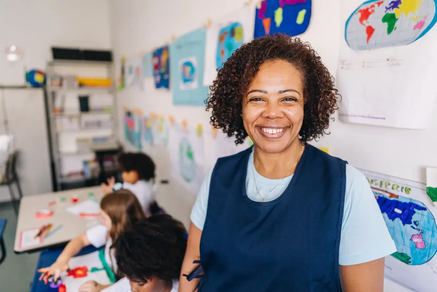 Profesora sonriendo en el aula, con estudiantes dibujando al fondo